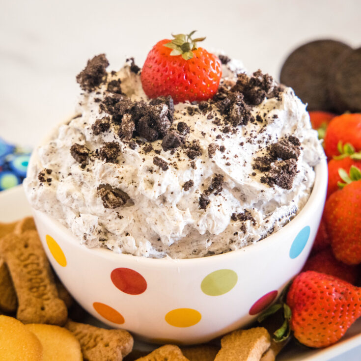 A bowl of Oreo fluff topped with crushed Oreos and a strawberry surrounded by a platter of dippables.
