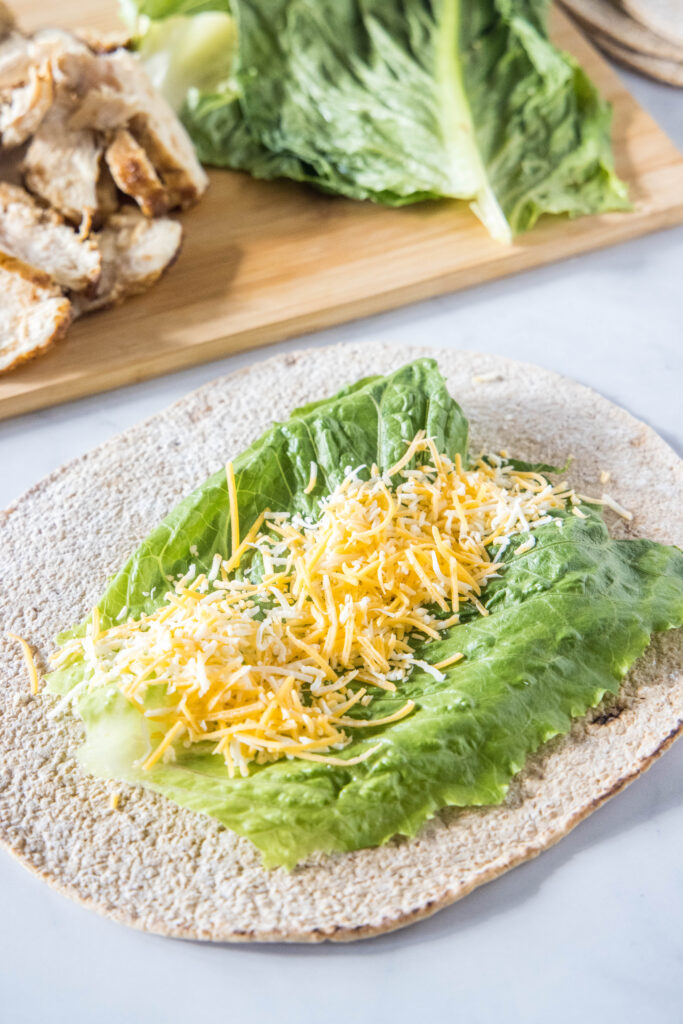 A tortilla wrap topped with a lettuce leaf and shredded cheese.