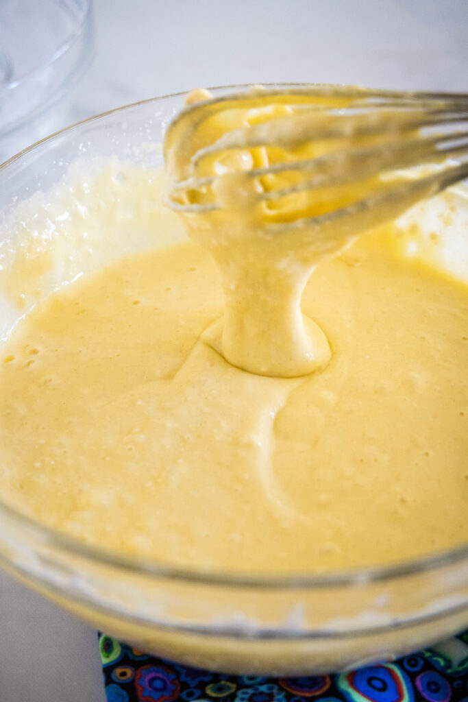 A whisk dripping ricotta pancake batter into a glass bowl.