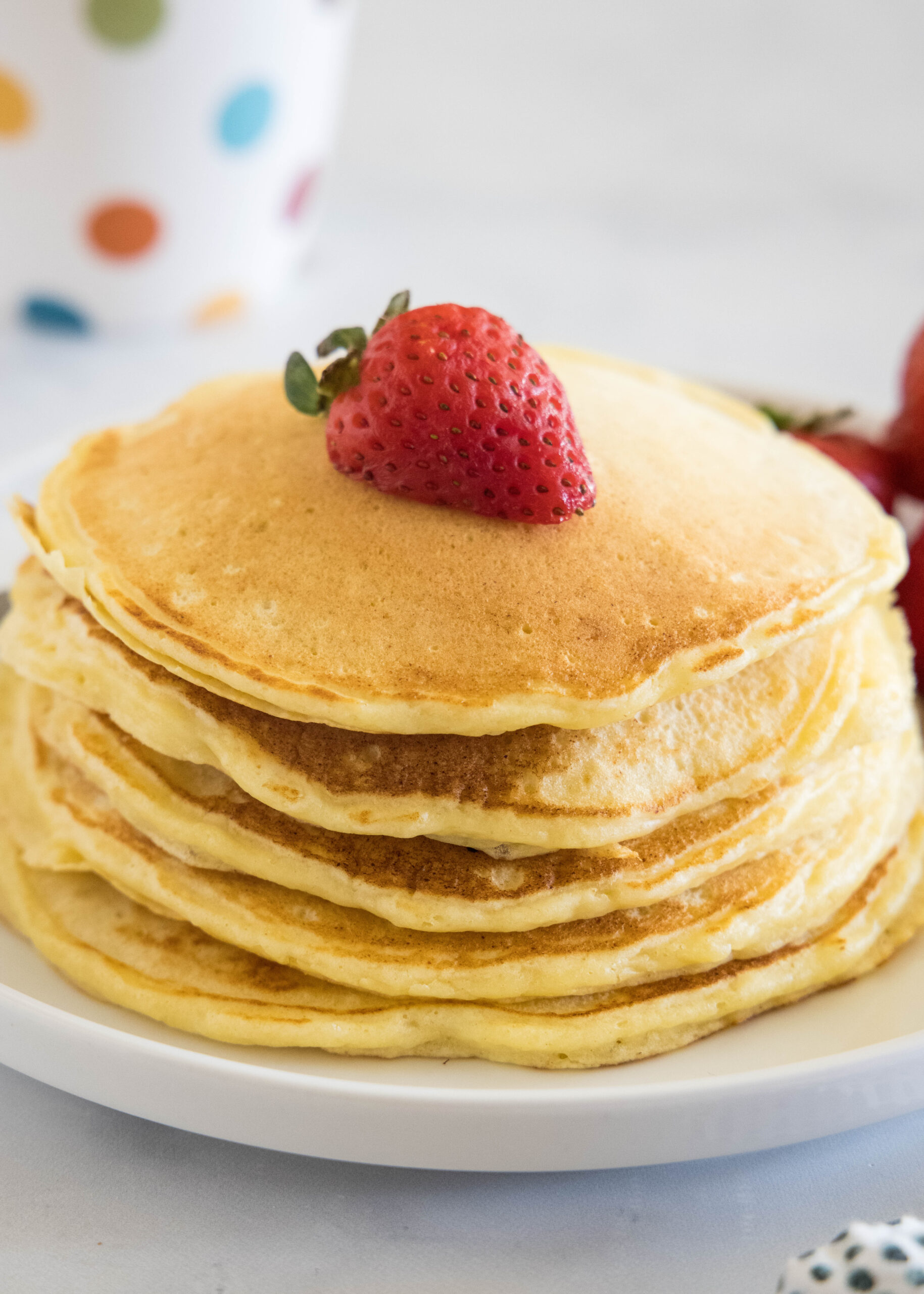 A stack of ricotta pancakes topped with a strawberry a plate.