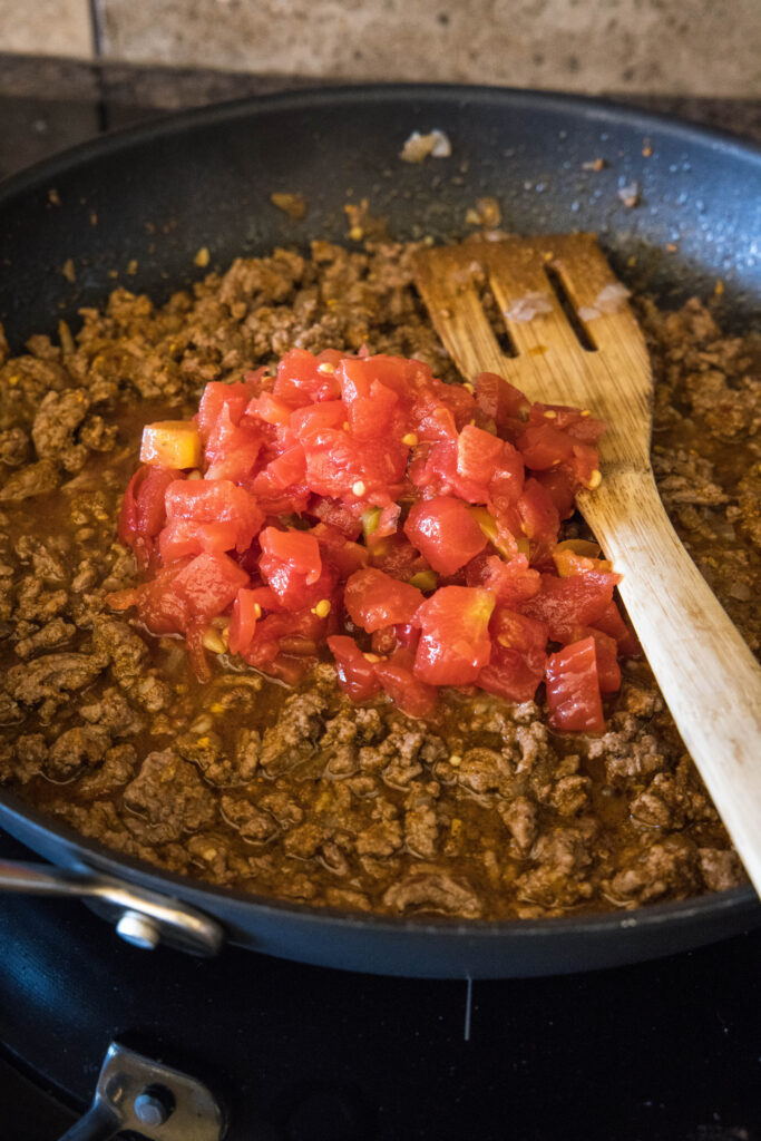 Canned tomatoes added to a skillet with taco meat.