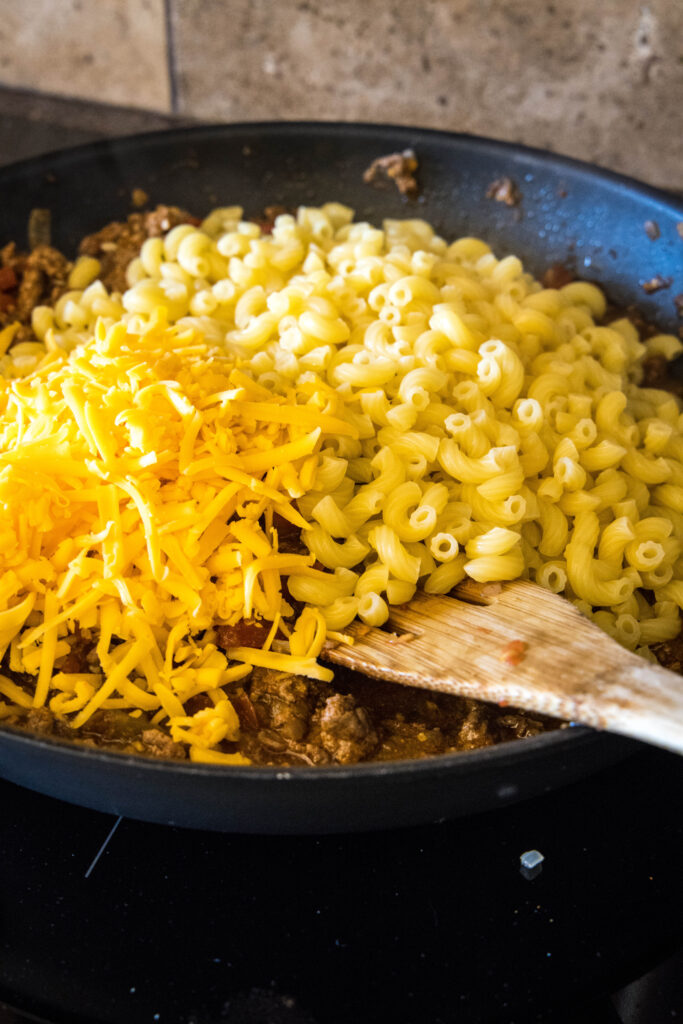 Cooked elbow macaroni noodles and shredded cheese added to a skillet with tao meat.