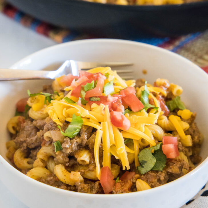 A bowl of taco mac and cheese with a skillet in the background.
