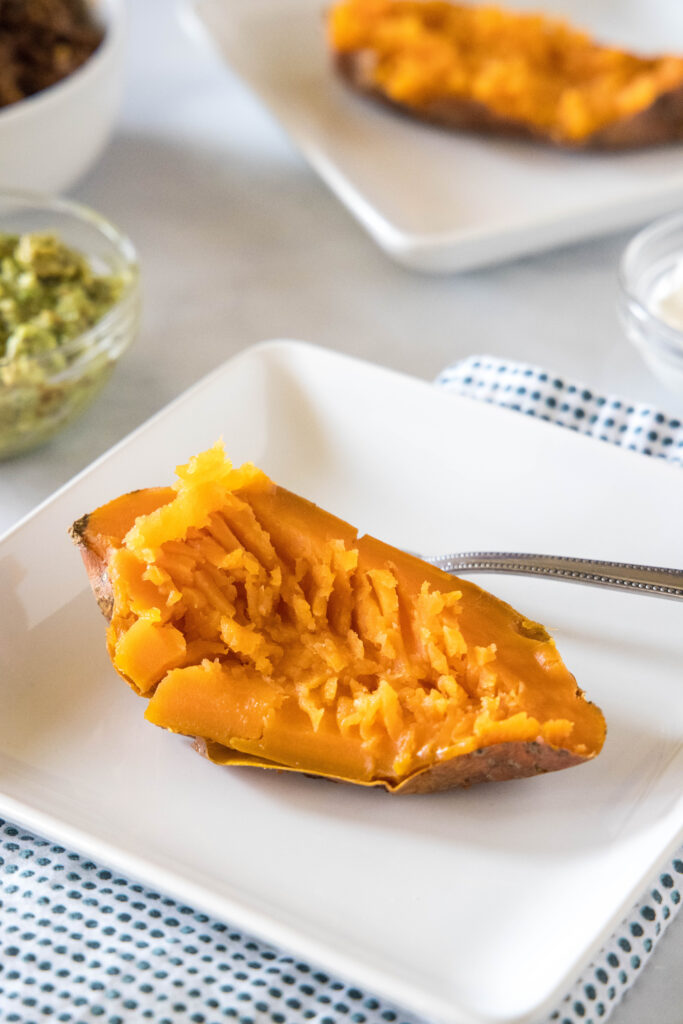 One half of a cooked sweet potato with the flesh fluffed on a white plate next to a fork.