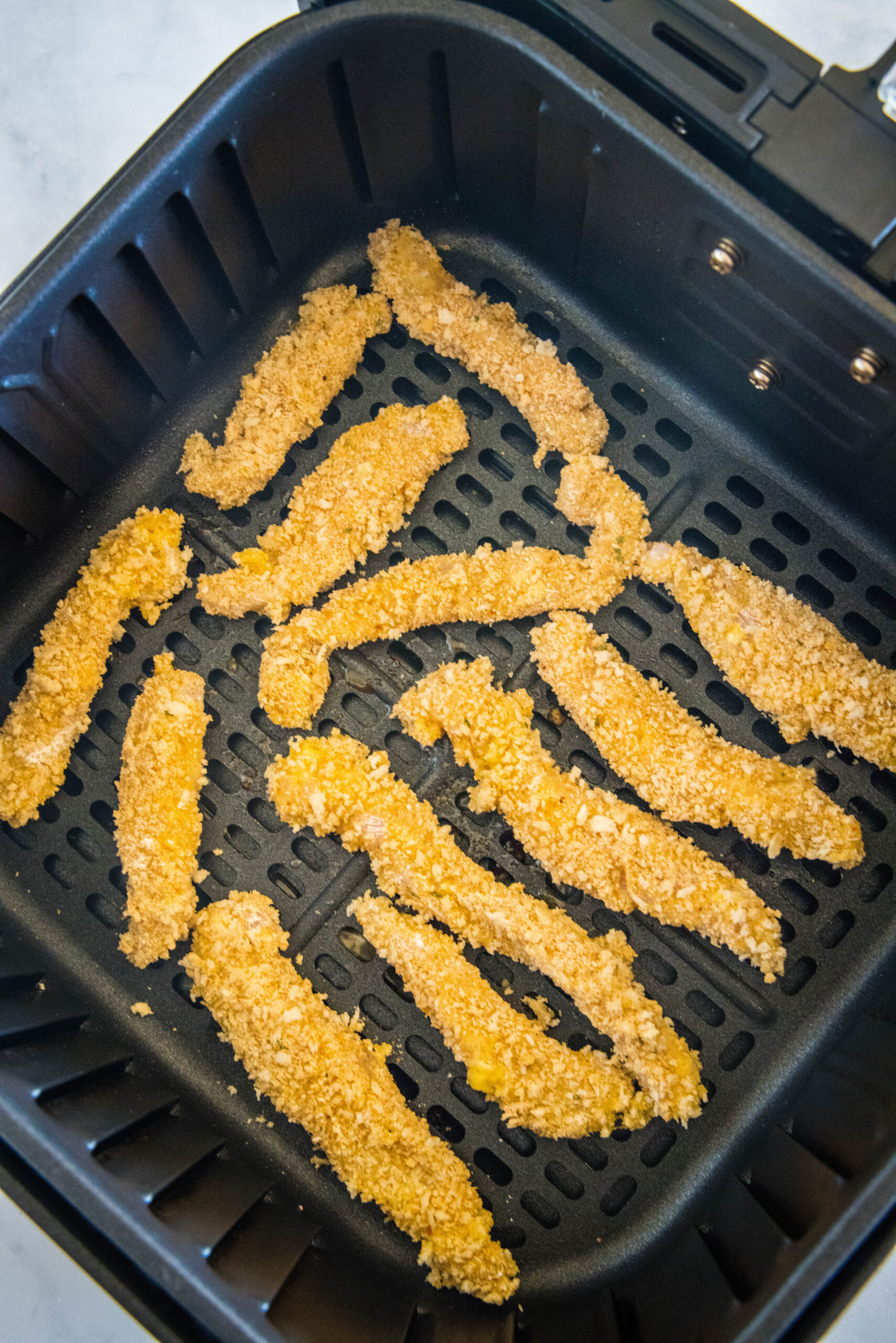 Overhead view of chicken fries inside the air fryer basket.