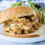 A slow cooker Hawaiian chicken sandwich on a plate, with a serving of green salad in the background.