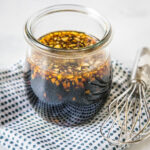Homemade teriyaki sauce in a glass jar on a blue and white polka dot napkin, next to a whisk.