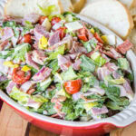 Hoagie dip in a red ceramic serving bowl with bread slices in the background.