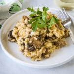 Sausage risotto garnished with fresh parsley on a white plate next to a fork.