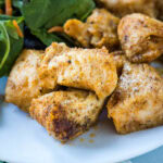 Close up of baked chicken bites next to green salad on a plate.