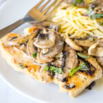 Chicken Marsala served on a plate next to spaghetti, topped with mushrooms.