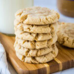 A stack of crunchy peanut butter cookies on a wooden cutting board.