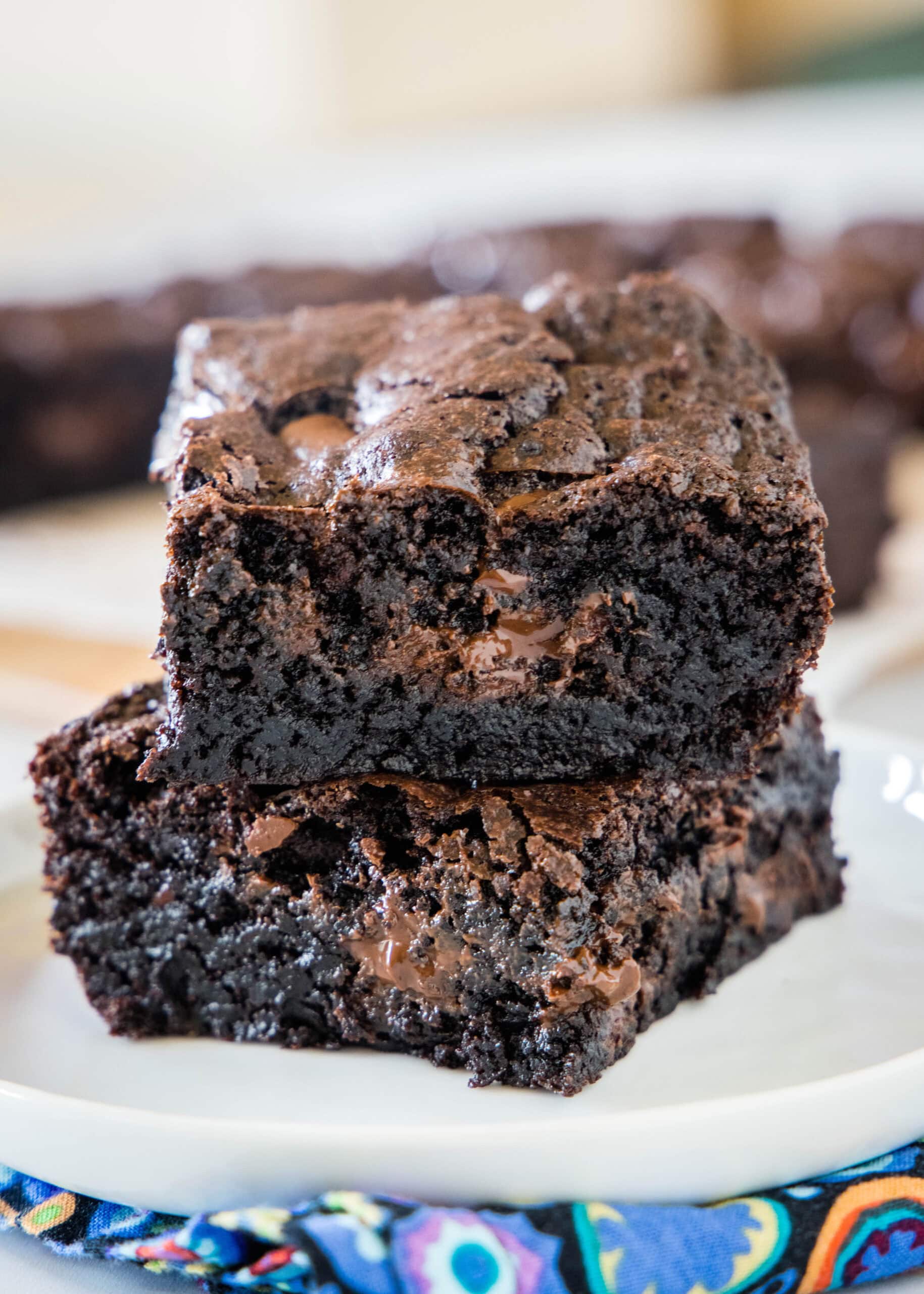 Make thick and chewy, fudgy double chocolate brownies with cocoa powder and chocolate chunks, for loads of melty chocolate in every bite! Two double chocolate brownies stacked on a plate.