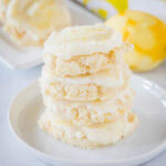Four frosted lemon sugar cookies stacked on a plate with a zested lemon in the background.
