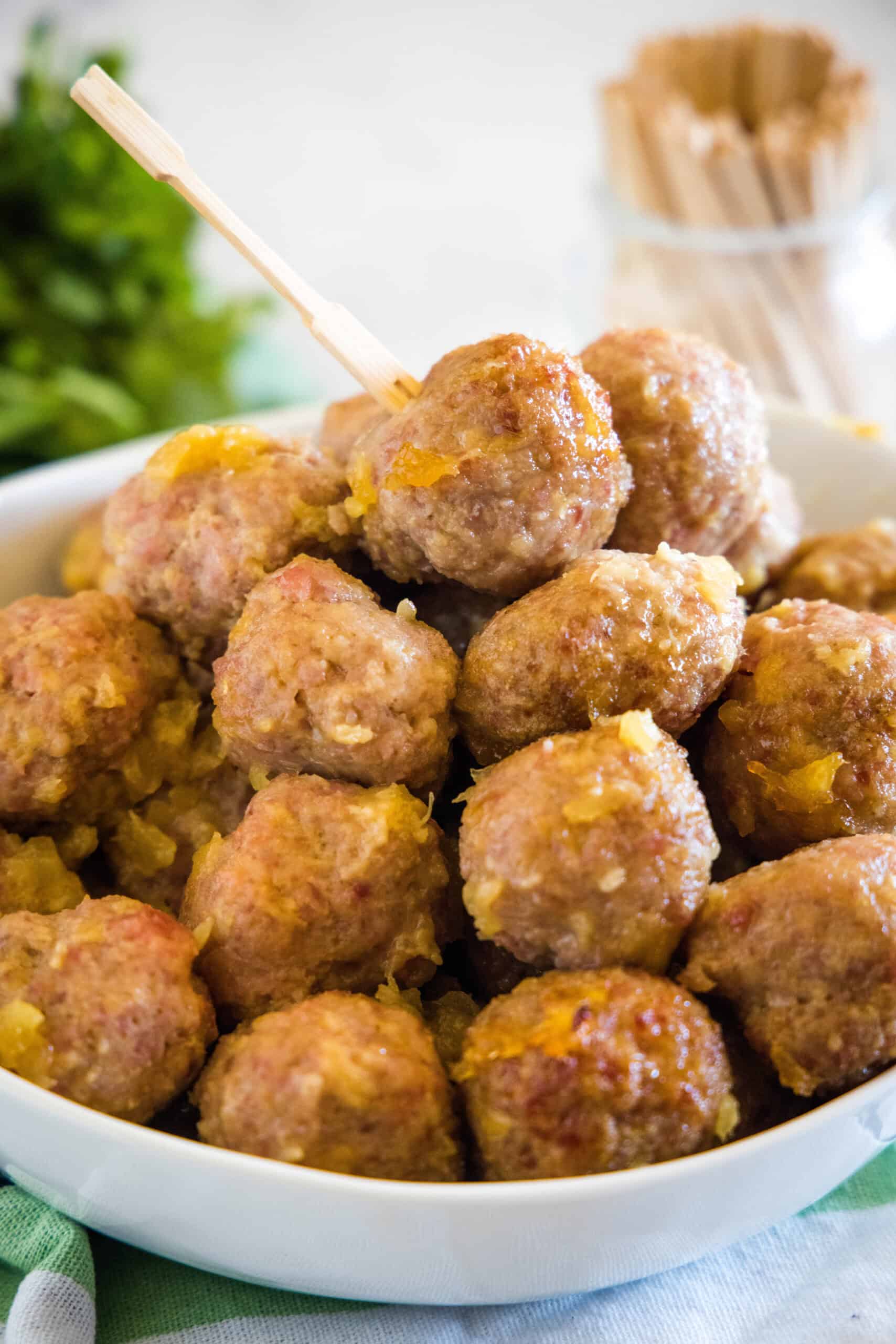 Ham balls with pineapple sauce piled into a bowl with a jar of cocktail skewers in the background.