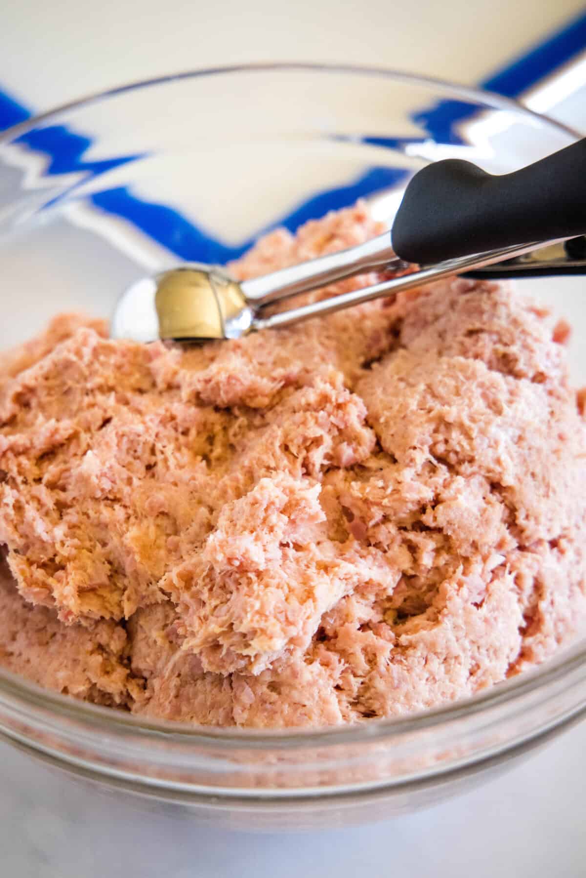 Ham meatball mixture in a glass bowl with a cookie scoop.