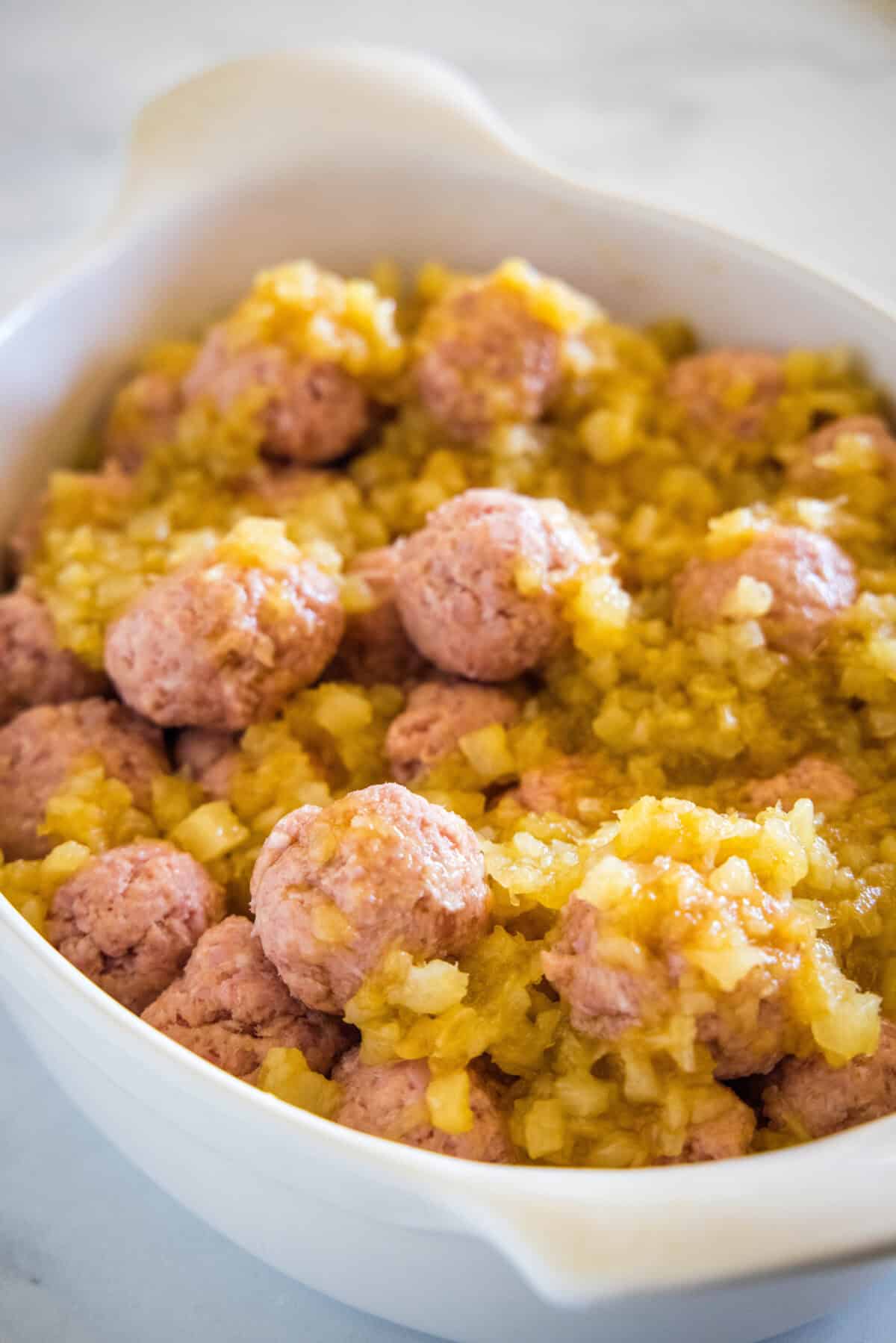 Unbaked ham balls covered with pineapple sauce in a ceramic baking dish.