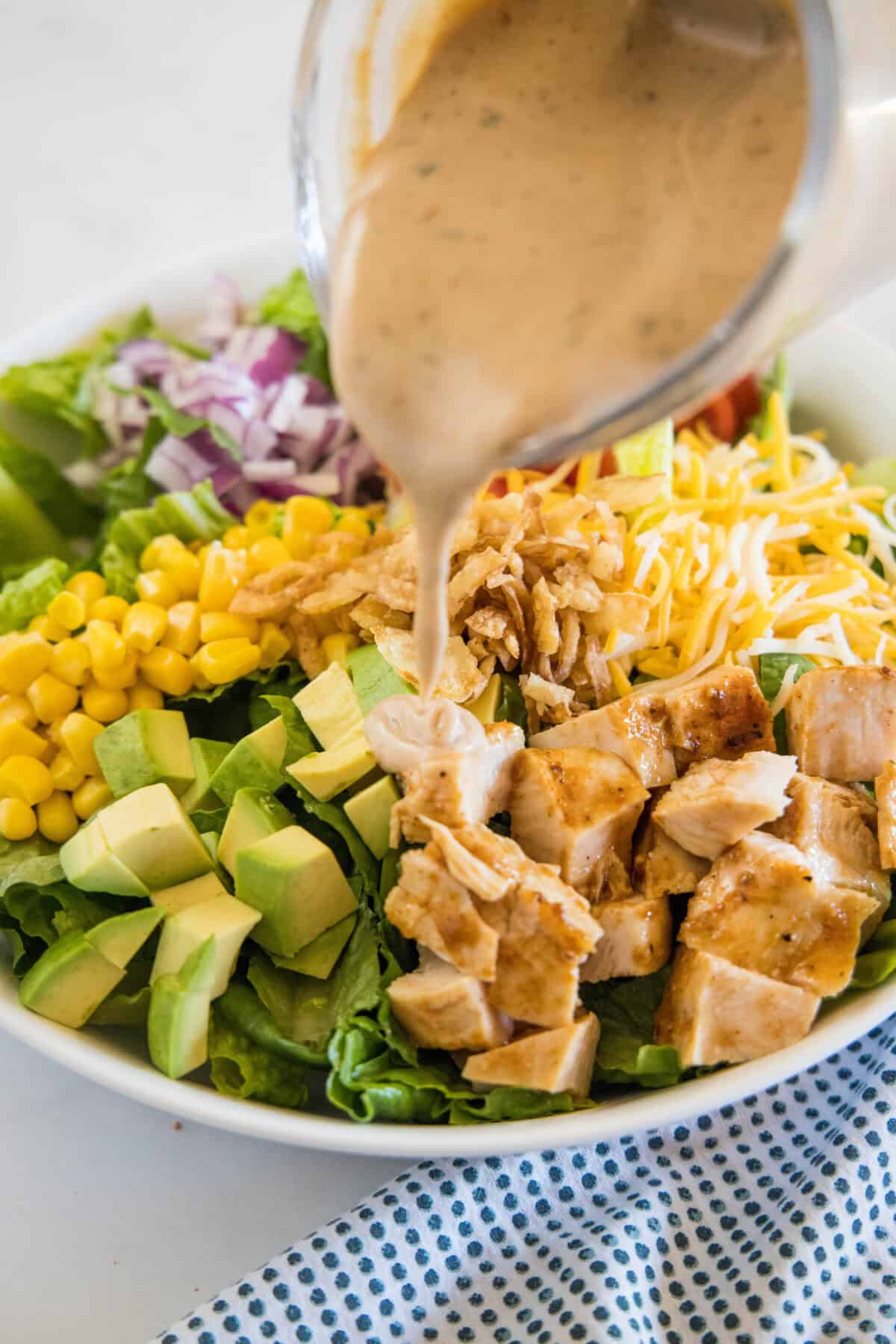 A spoon drizzling barbecue ranch dressing over a BBQ chicken salad assembled in a bowl.