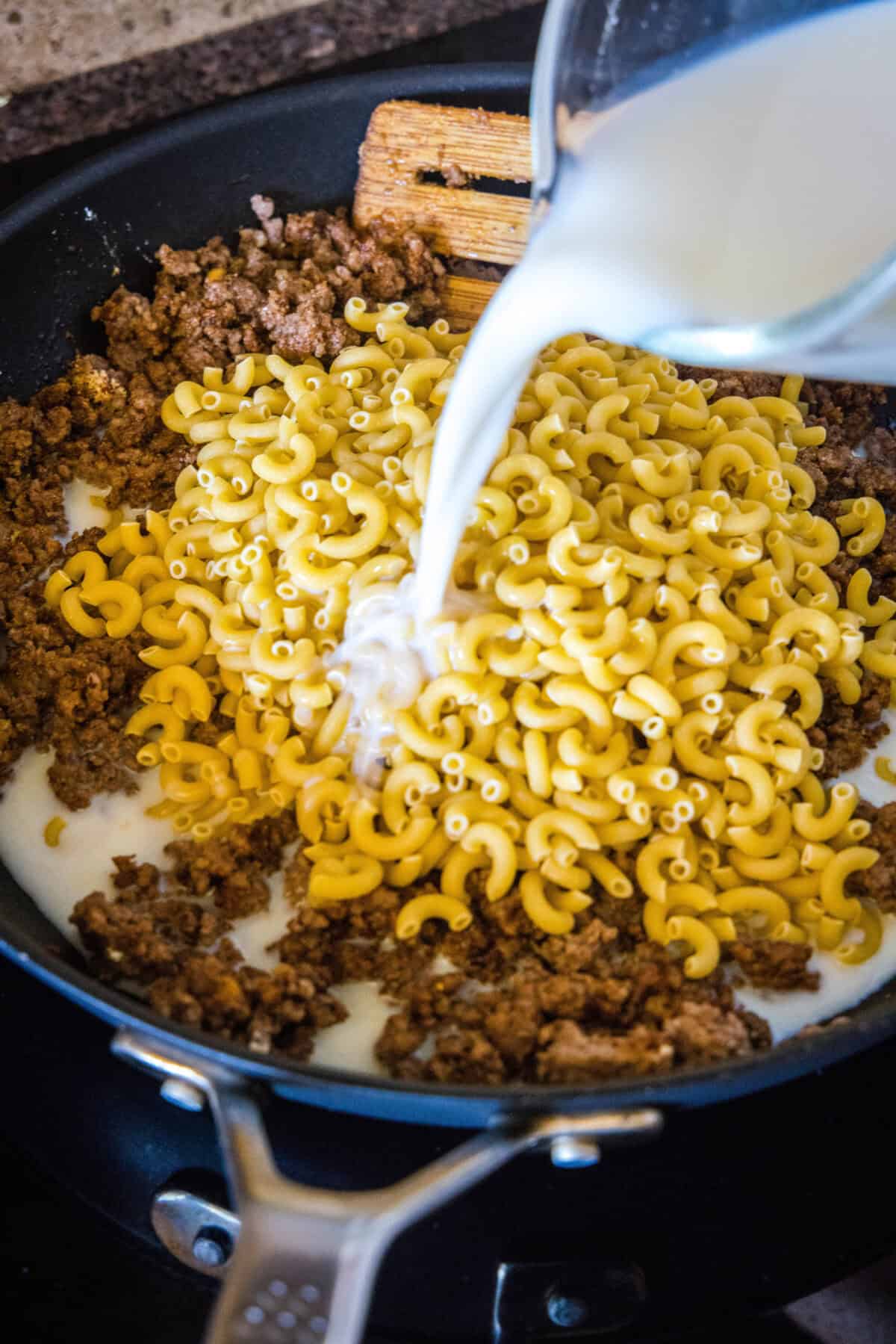 pouring milk into skillet with pasta