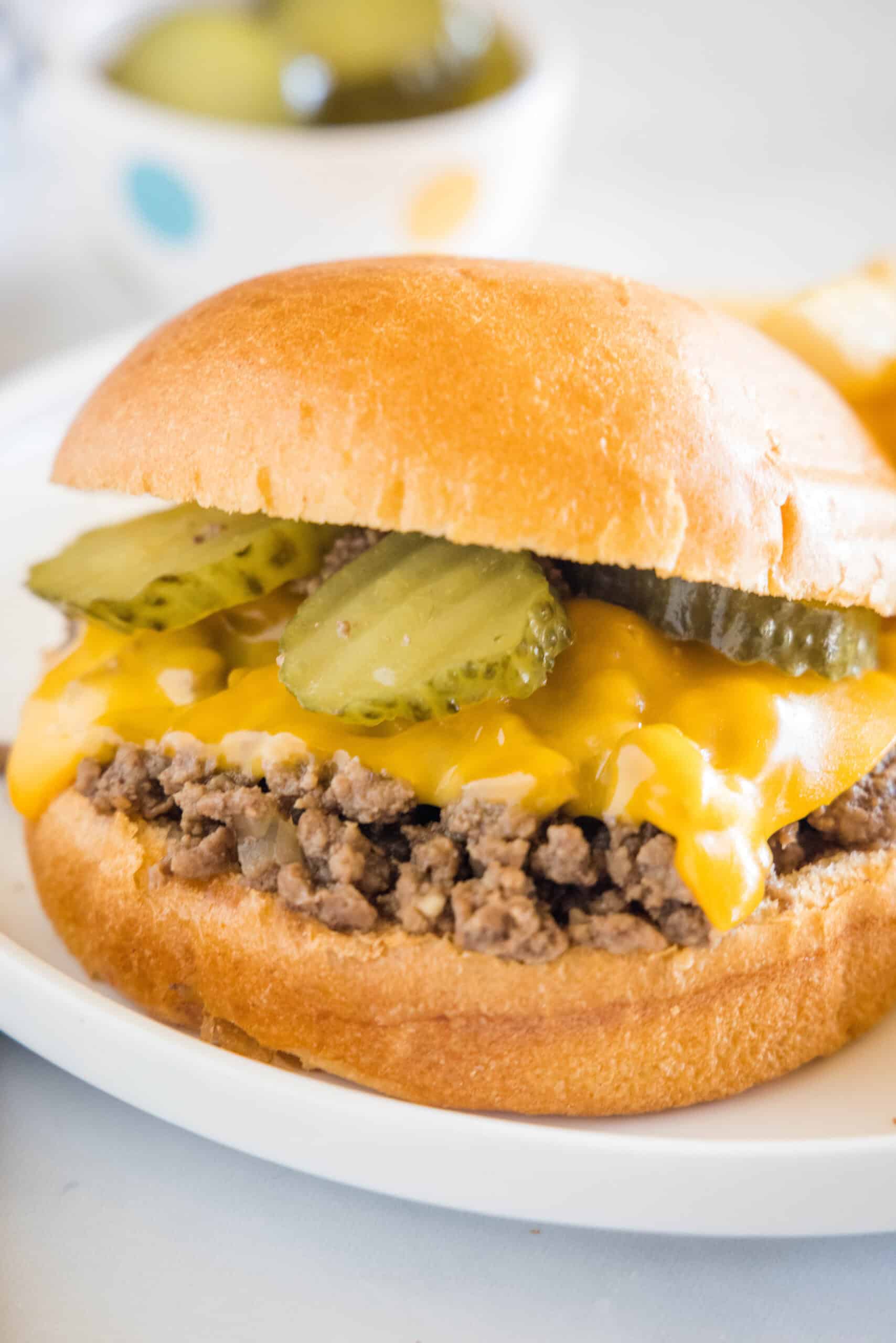 A Maid Rite sandwich garnished with pickles and melted cheese on a white plate.