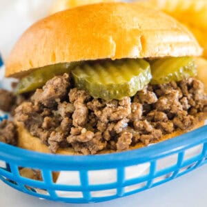 Close up of a Maid Rite loose meat sandwich garnished with pickles in a blue plastic serving basket.