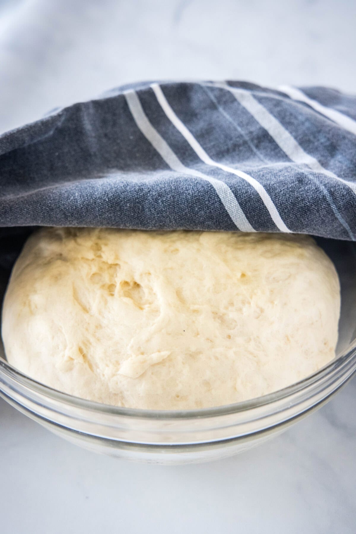 Risen bread dough underneath a dishcloth in a glass bowl.
