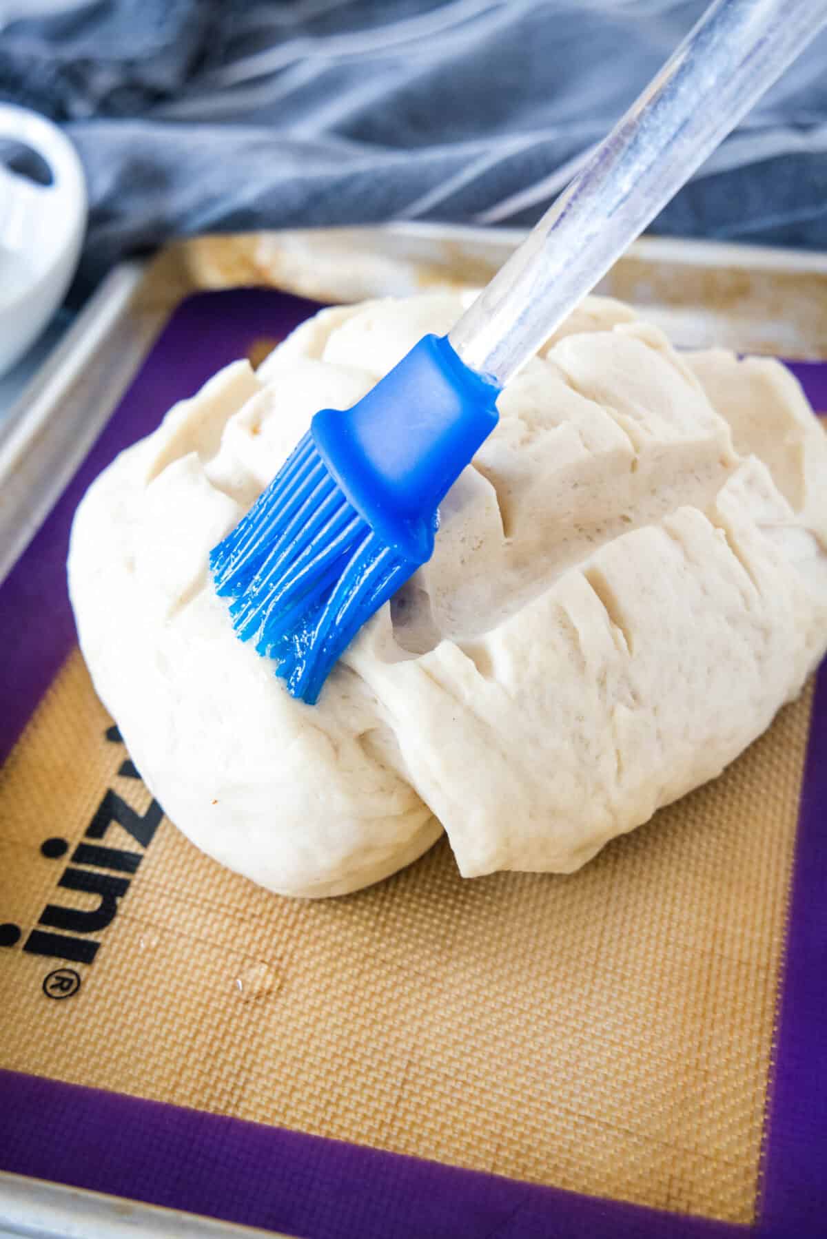 A basting brush coating scored bread dough with egg wash.
