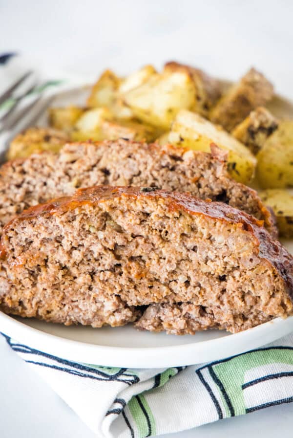 Onion soup meatloaf slices on a plate with roasted potatoes in the background.