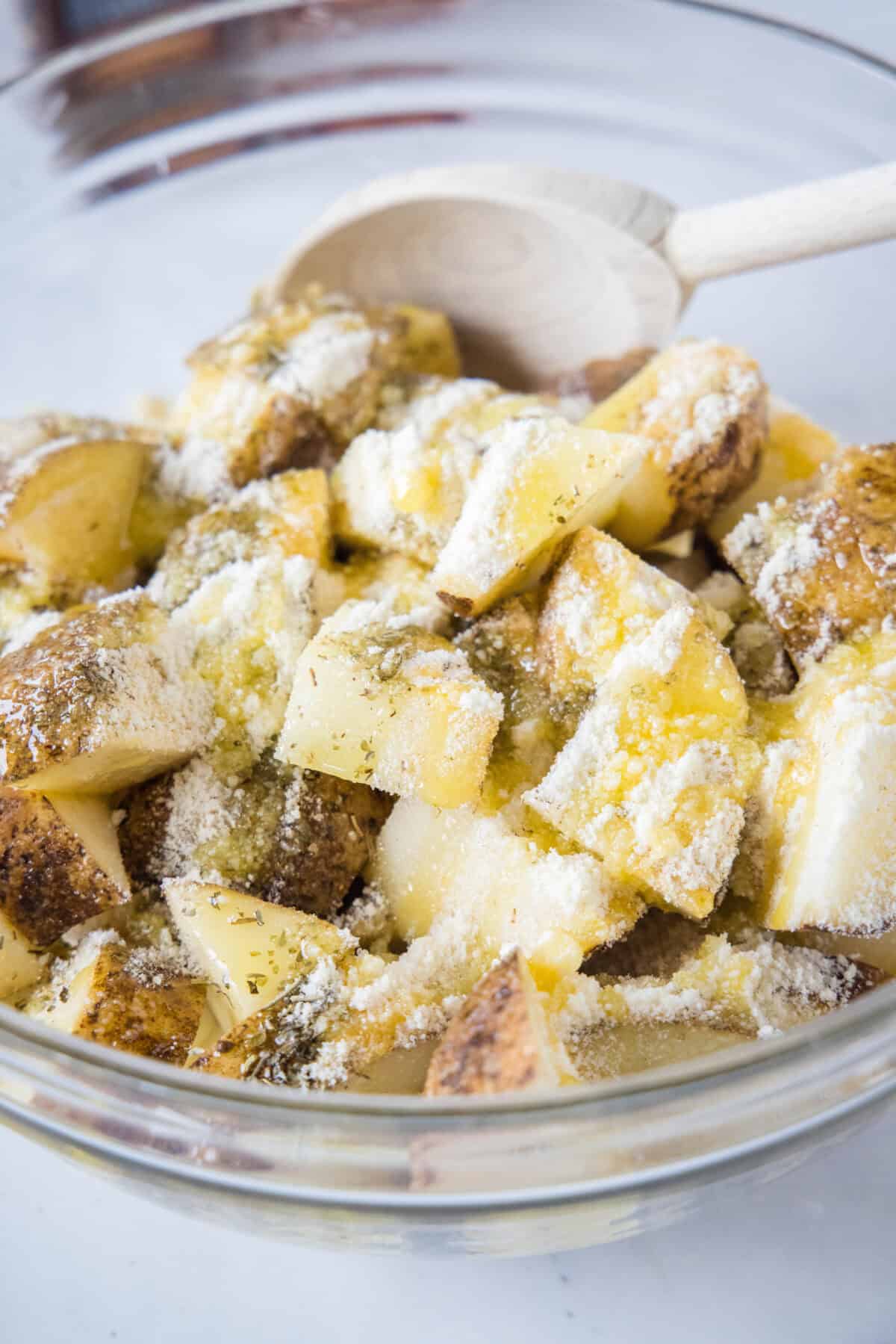 Cubed potatoes tossed with olive oil and seasonings in a bowl.