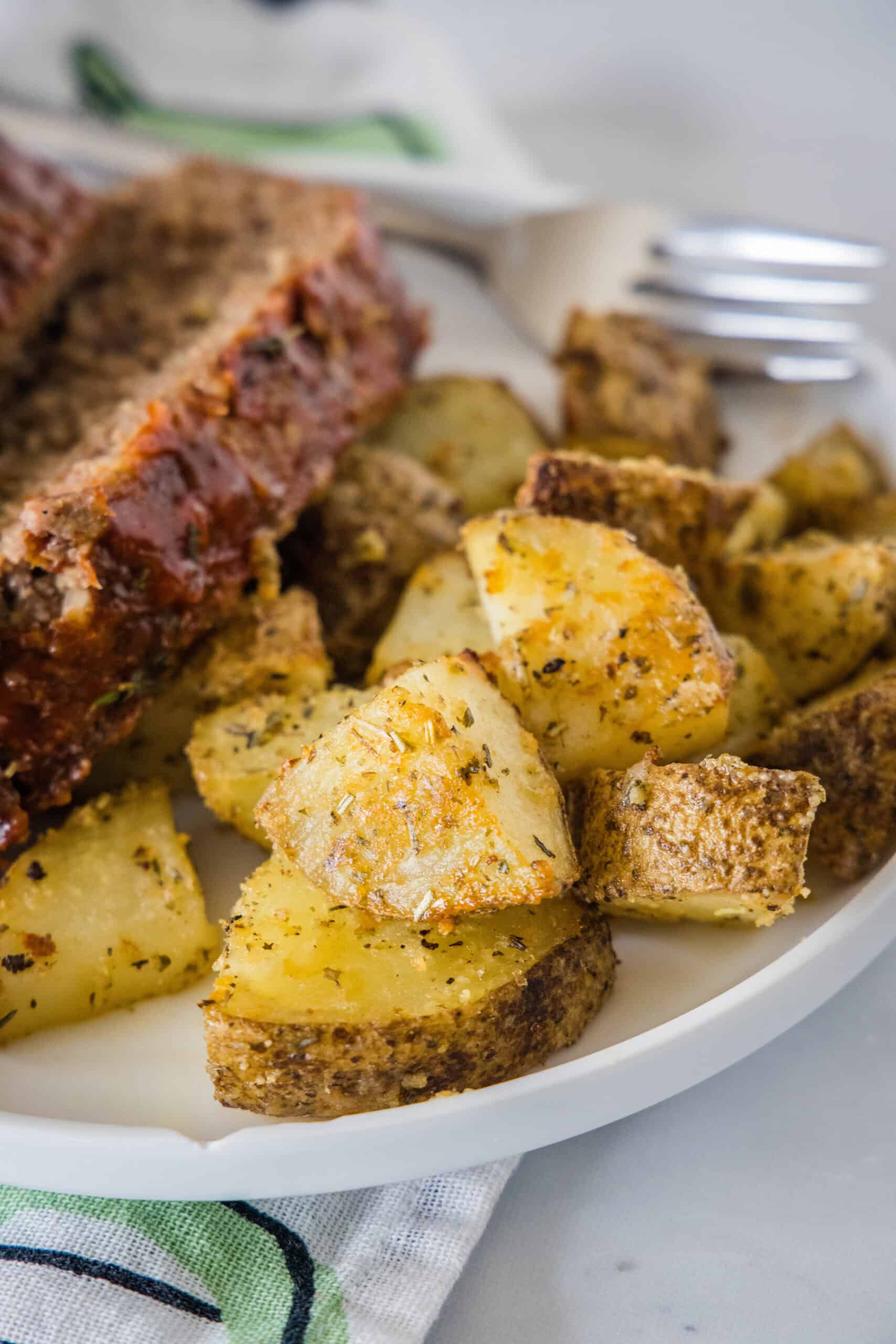 Make perfectly golden, crispy oven roasted potatoes as an easy side dish or appetizer! All it takes is olive oil and a handful of spices. Close up of seasoned oven roasted potatoes on a plate.