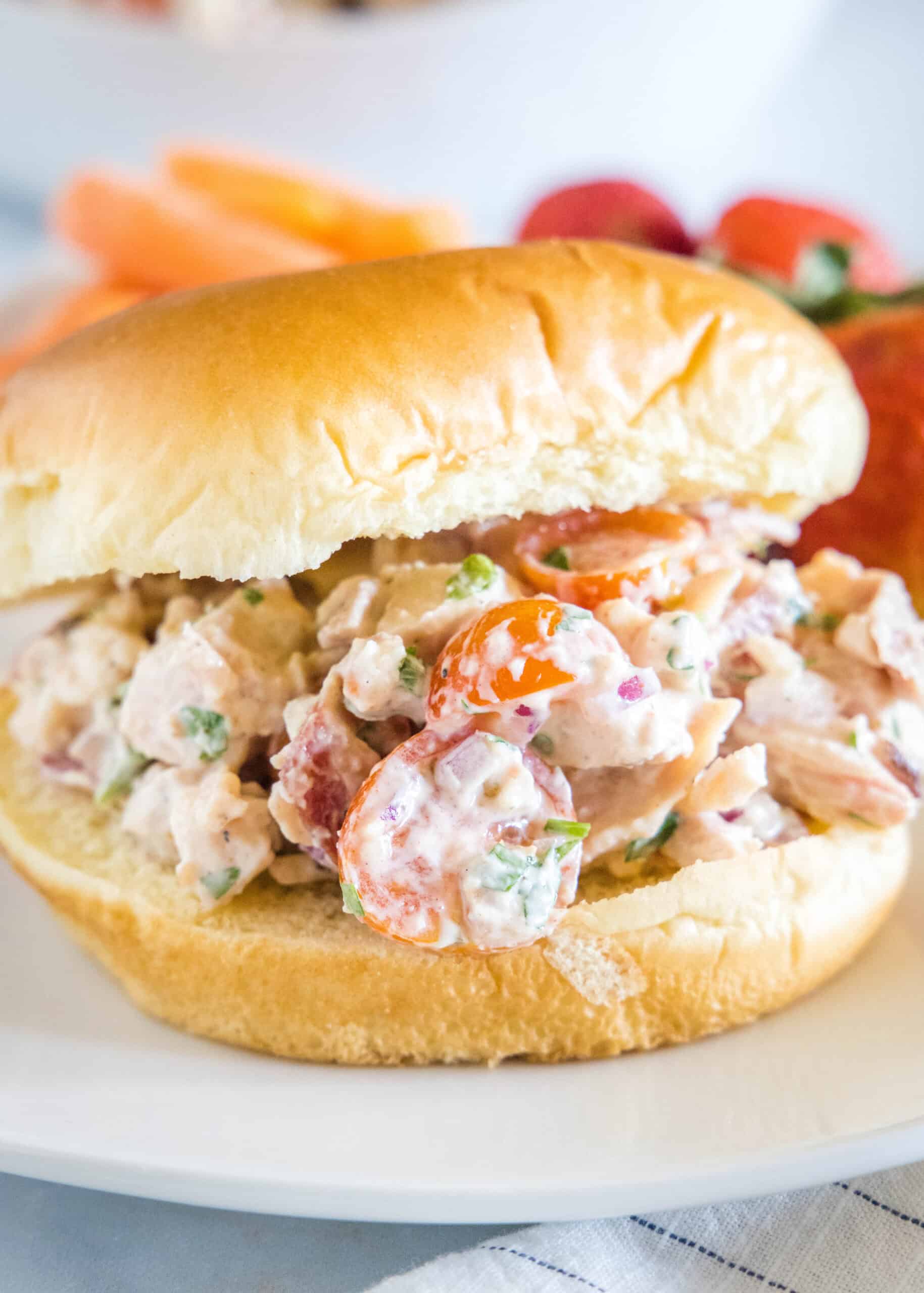 This BLT chicken salad is loaded with juicy shredded chicken, bacon, cherry tomatoes, and crispy red onion tossed with creamy mayo dressing. A BLT chicken salad sandwich on a fluffy bun on a white plate.