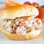 A BLT chicken salad sandwich on a fluffy bun on a white plate.