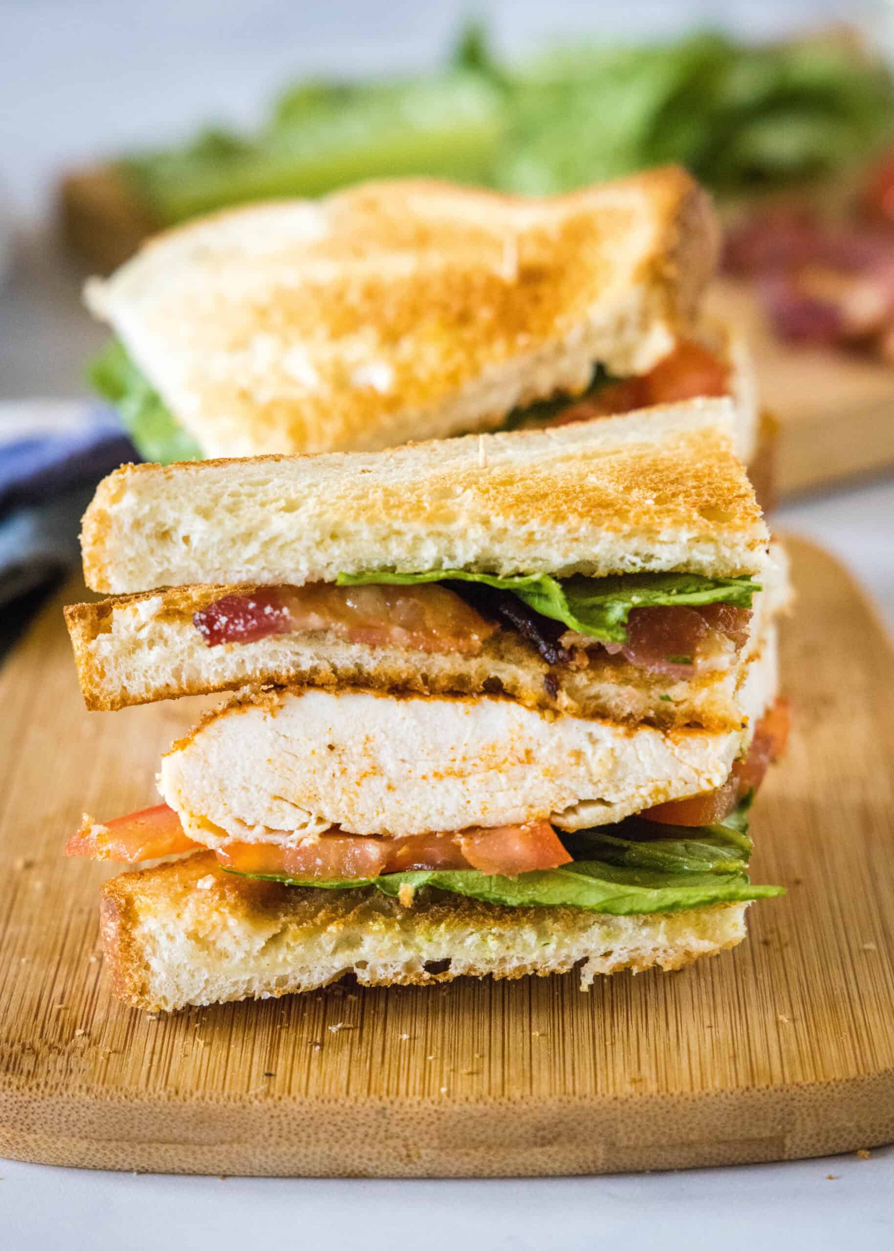 Close up of one half of a chicken club sandwich on a wooden cutting board.