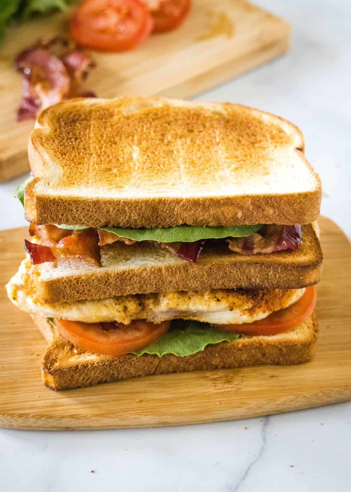 A chicken club sandwich assembled on a wooden cutting board.