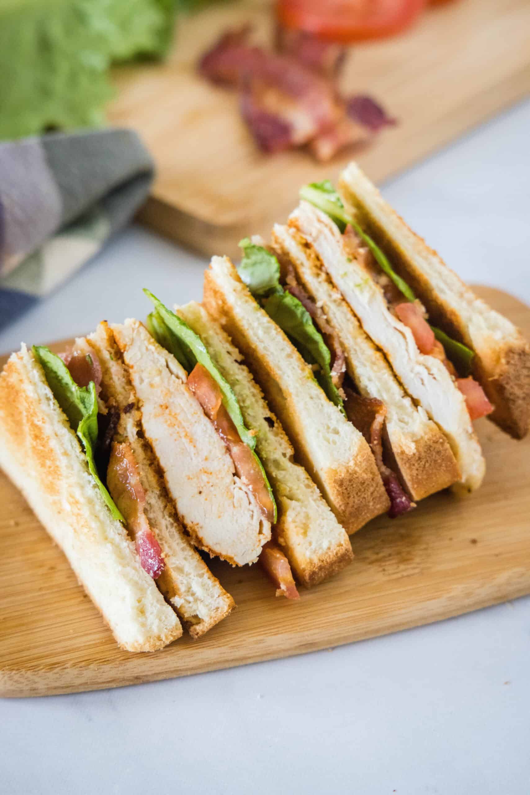 A chicken club sandwich cut into two halves on a wooden cutting board.