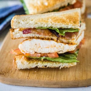 Close up of one half of a chicken club sandwich on a wooden cutting board.