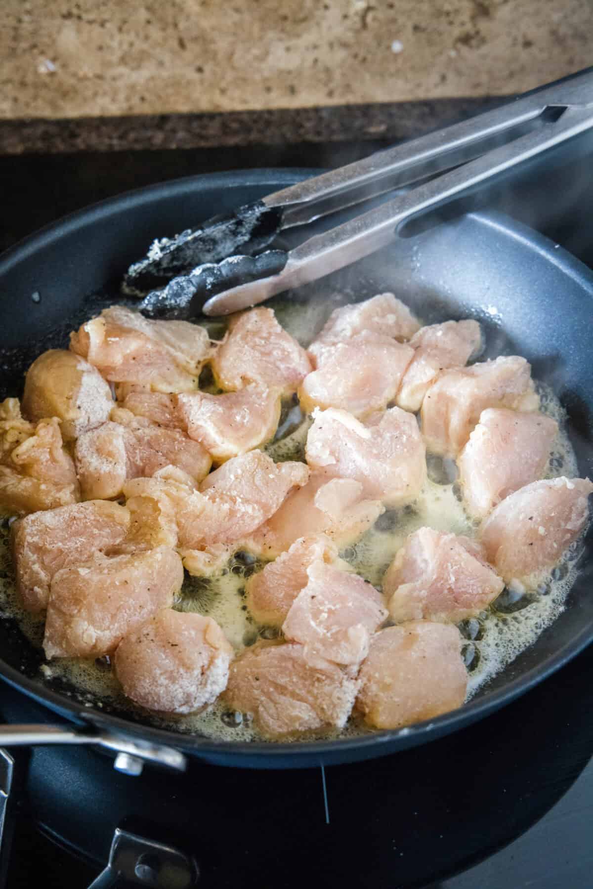 This chicken scampi recipe is a quick, easy chicken pasta with juicy chicken bites cooked in a buttery white wine sauce with garlic and lemon. Chicken pieces sautéing in a skillet.