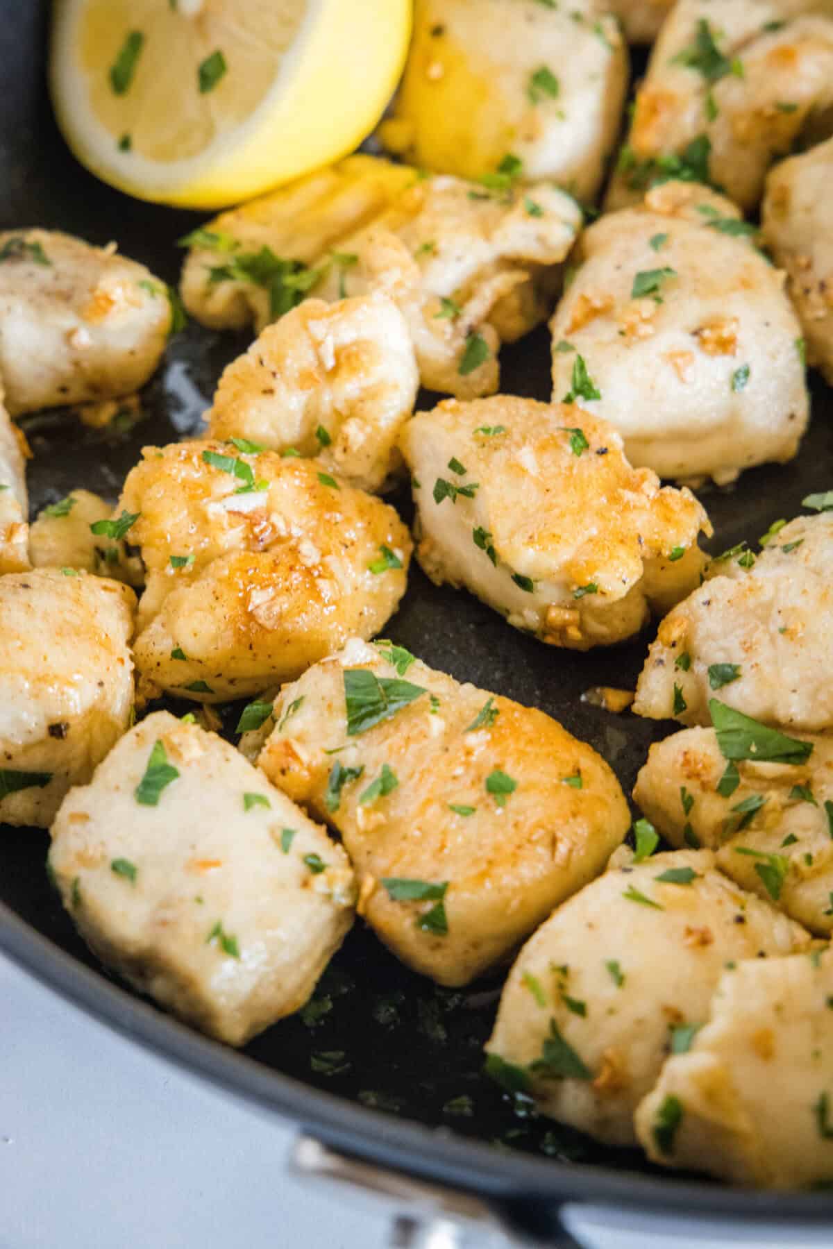 This chicken scampi recipe is a quick, easy chicken pasta with juicy chicken bites cooked in a buttery white wine sauce with garlic and lemon. Close up of seared chicken pieces garnished with parsley in a skillet.
