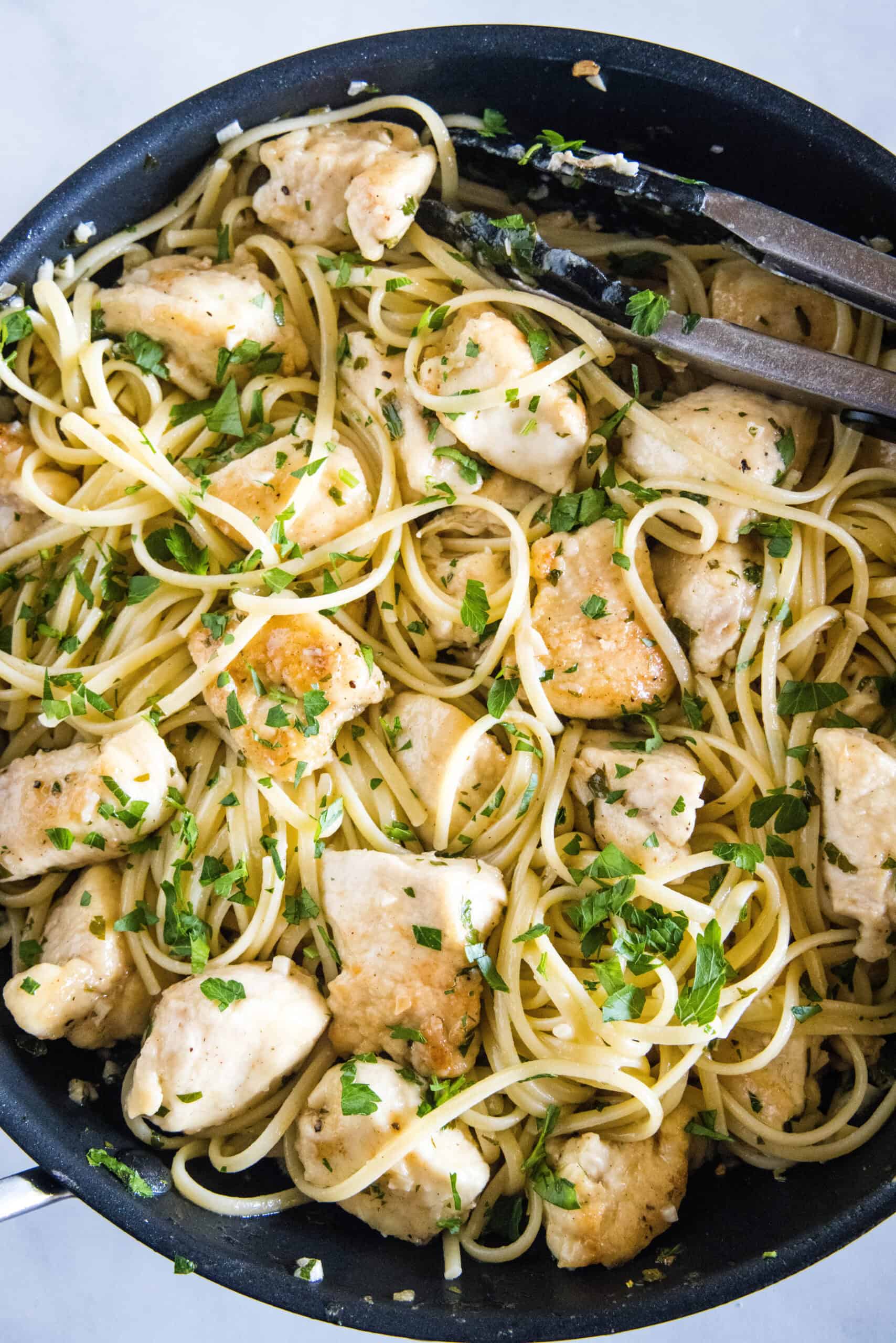 This chicken scampi recipe is a quick, easy chicken pasta with juicy chicken bites cooked in a buttery white wine sauce with garlic and lemon. Overhead view of chicken scampi with spaghetti in a skillet.