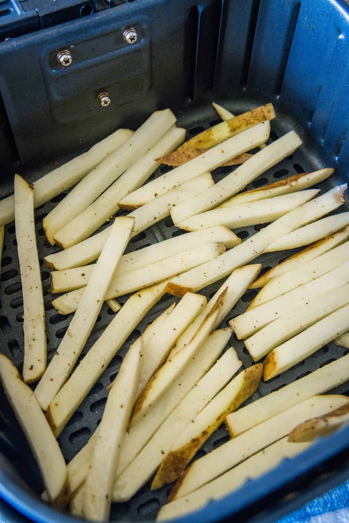 Homemade air fryer French fries are just as crispy as regular fries! Make them in a fraction of the time, with any seasonings you’d like. Uncooked homemade French fries inside the air fryer basket.
