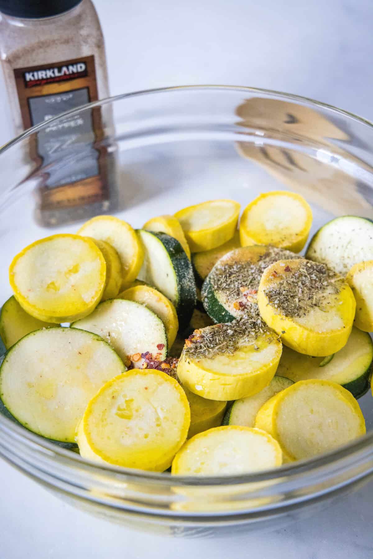 Make perfectly tender-crisp roasted zucchini and squash in the oven. It's an easy vegetable side dish that's ready in 20 minutes! Seasonings added to sliced zucchini and squash in a glass bowll.