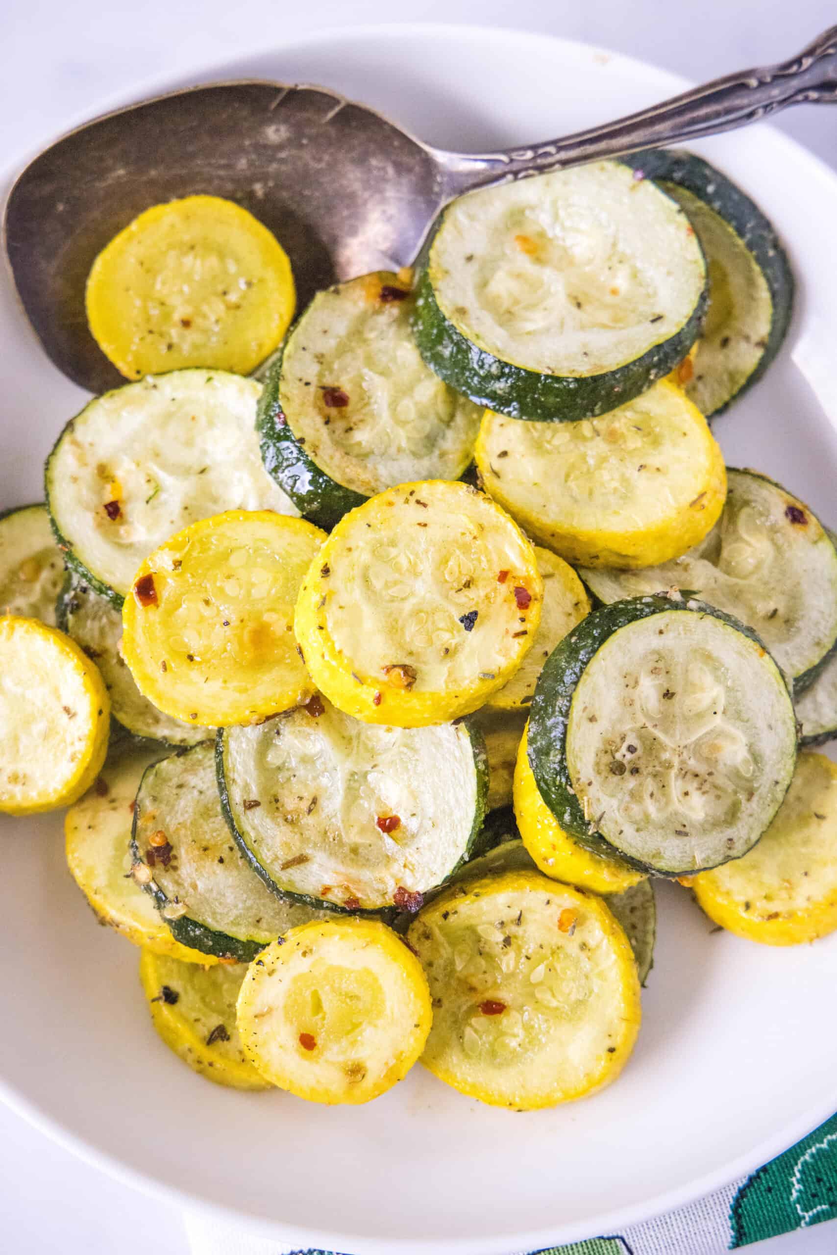 Make perfectly tender-crisp roasted zucchini and squash in the oven. It's an easy vegetable side dish that's ready in 20 minutes! Overhead view of roasted zucchini and squash in a bowl with a serving spoon.