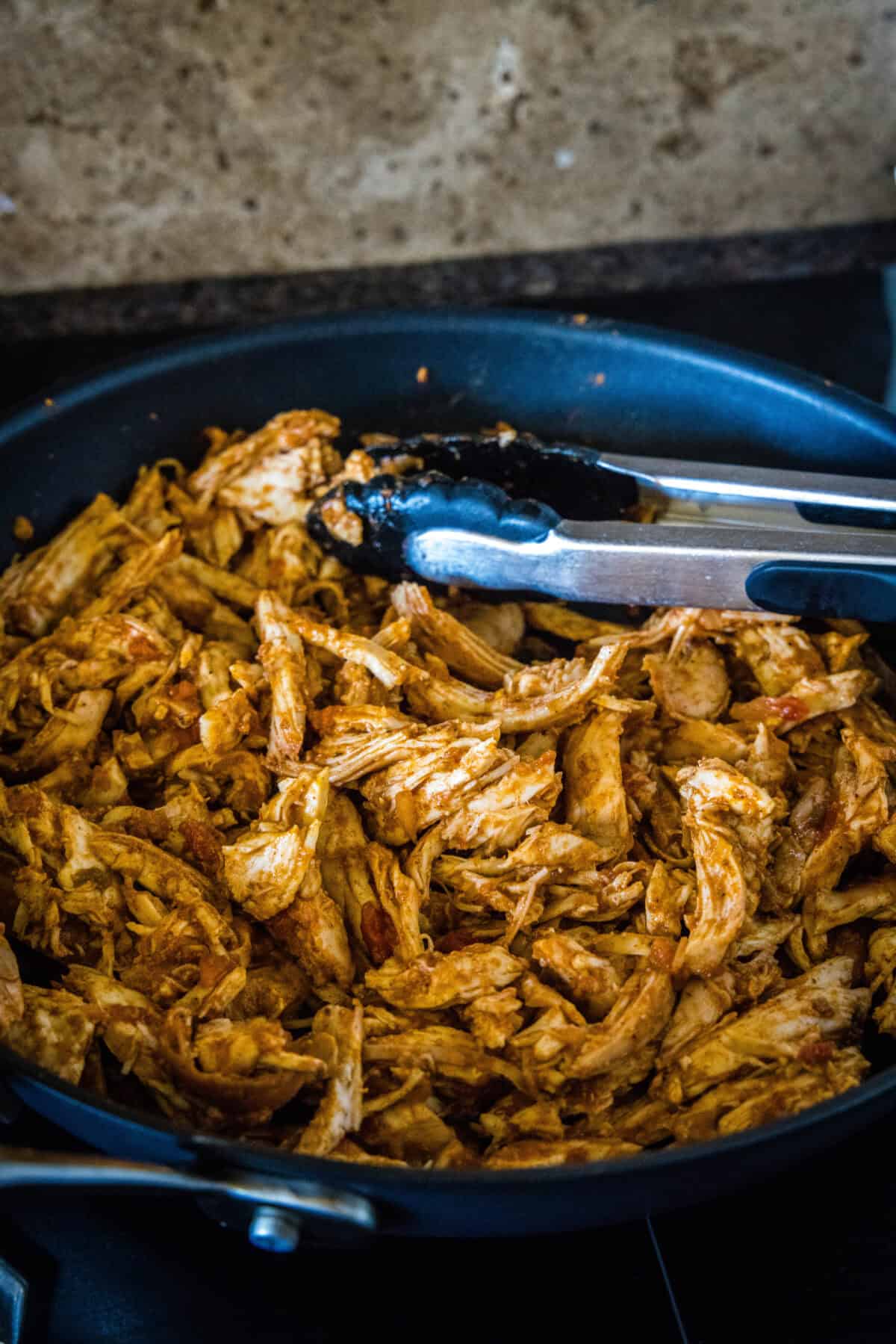 Juicy rotisserie chicken tacos are the best shortcut on taco night! Make delicious, easy chicken tacos in 15 minutes with only 3 ingredients. Shredded salsa rotisserie chicken in a skillet with a set of tongs.
