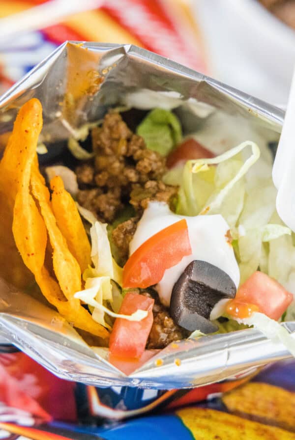 A walking taco topped wth lettuce, tomatoes, and sour cream inside a chip bag with a fork.