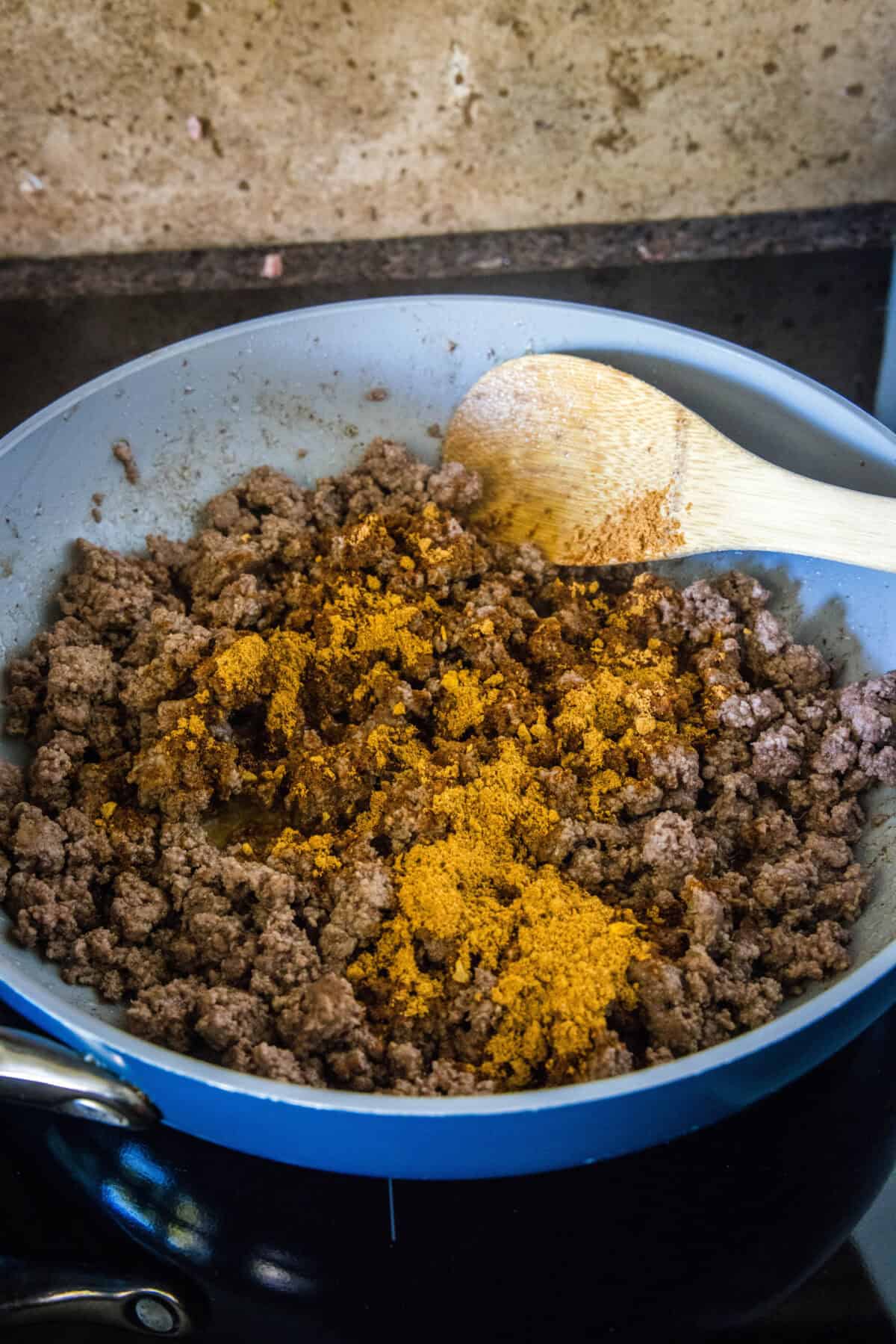 adding taco seasoning to ground beef in a skillet