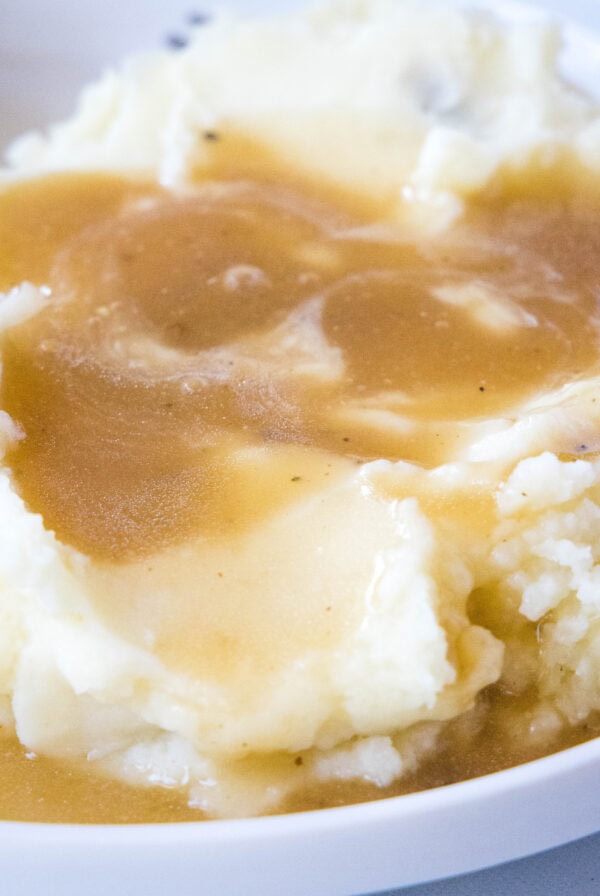 close up of brown gravy over mashed potatoes on a white plate