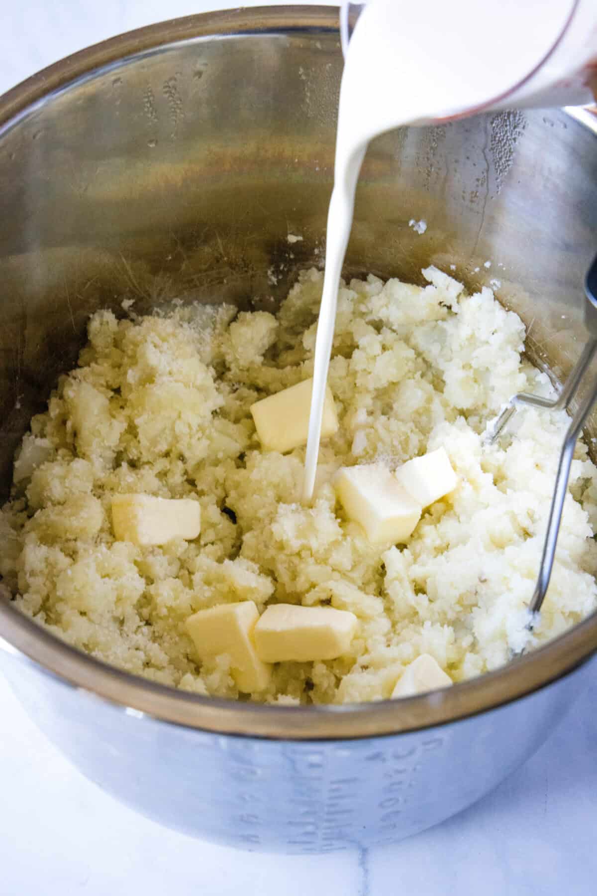 pouring heavy cream and butter into cooked potatoes