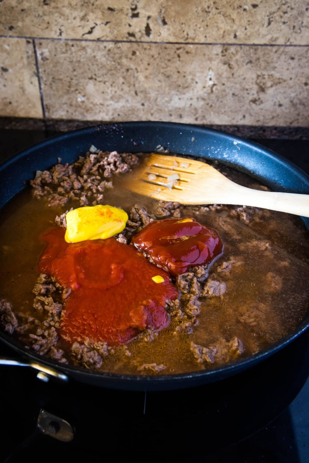adding tomato and mustard to skillet with ground beef