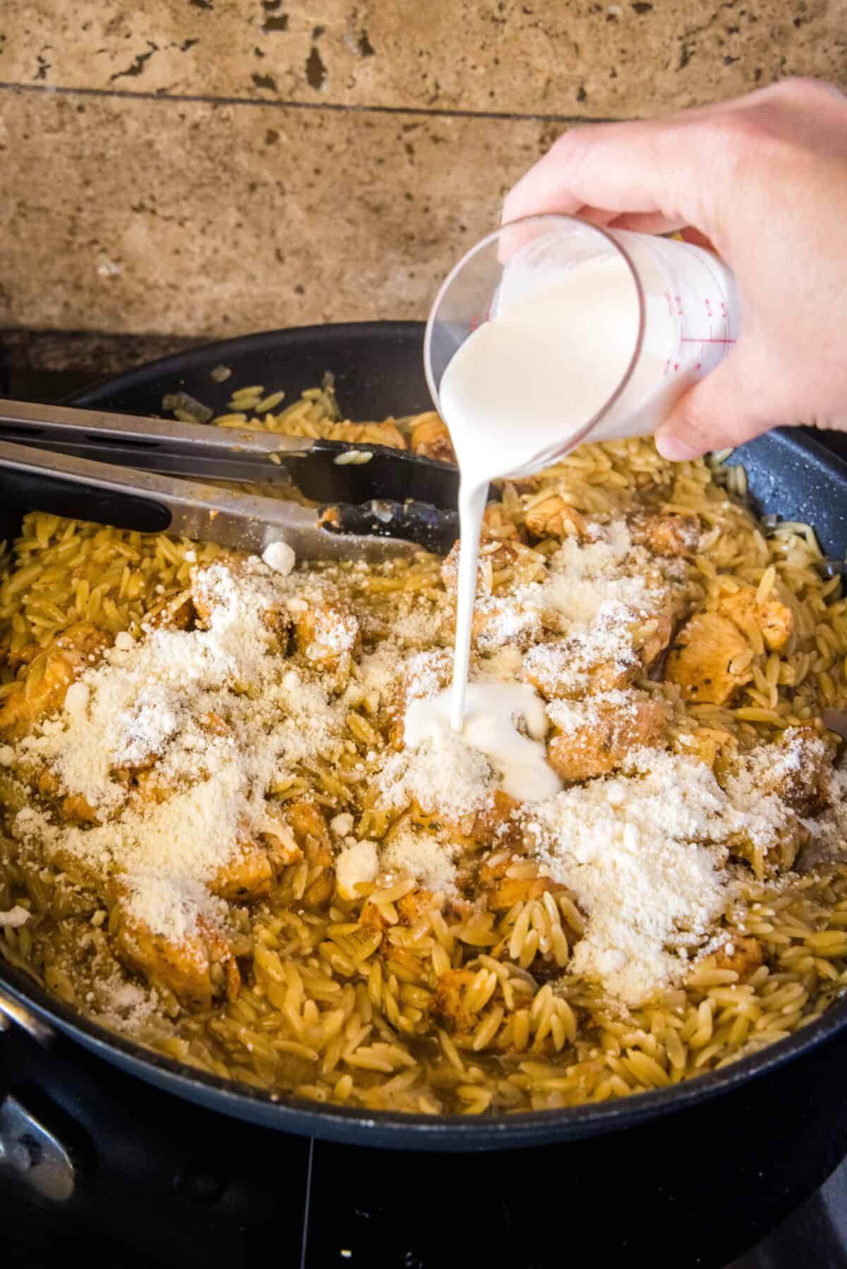 pouring heavy cream and Parmesan cheese to skillet with orzo