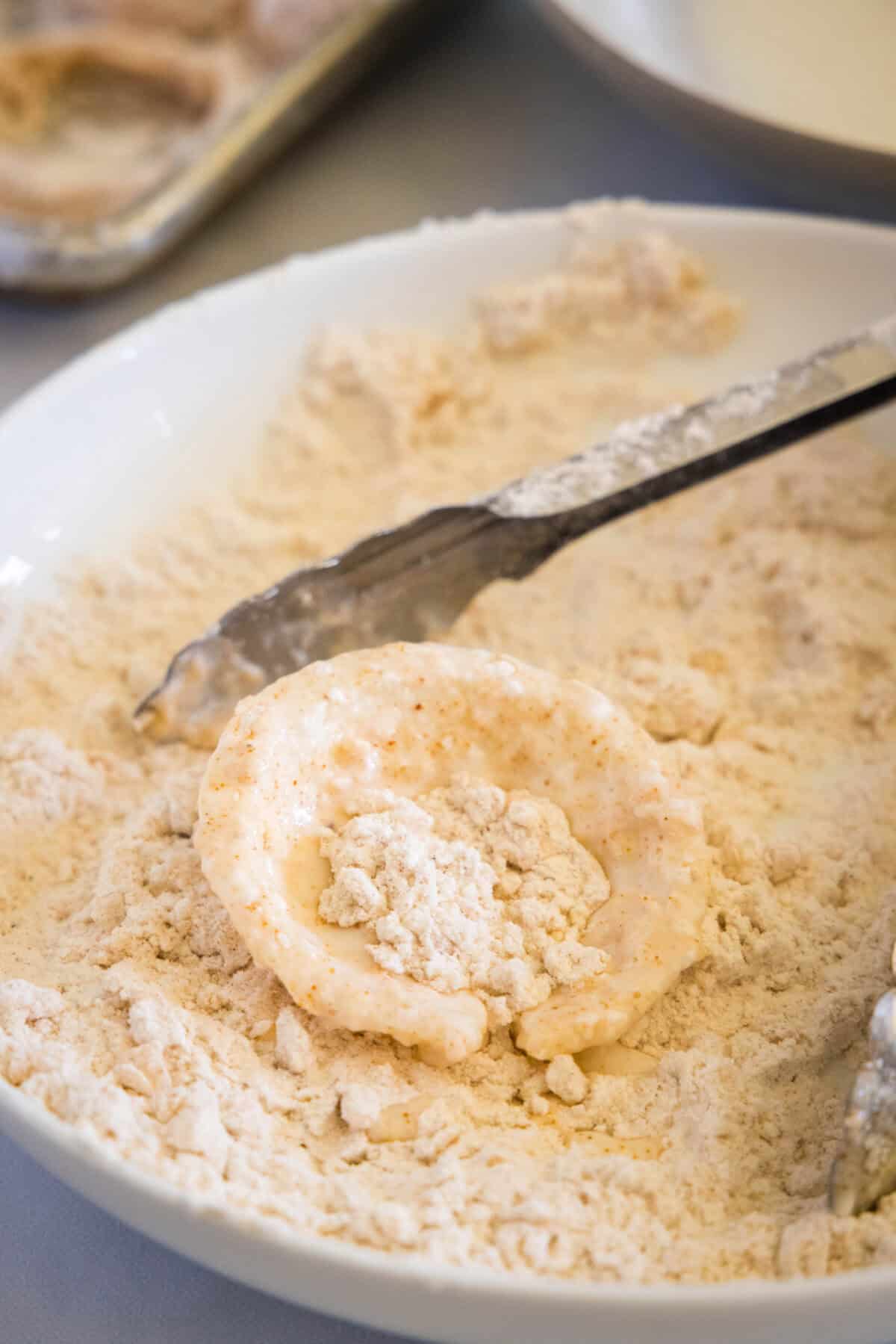 breading onion ring in bowl of lour